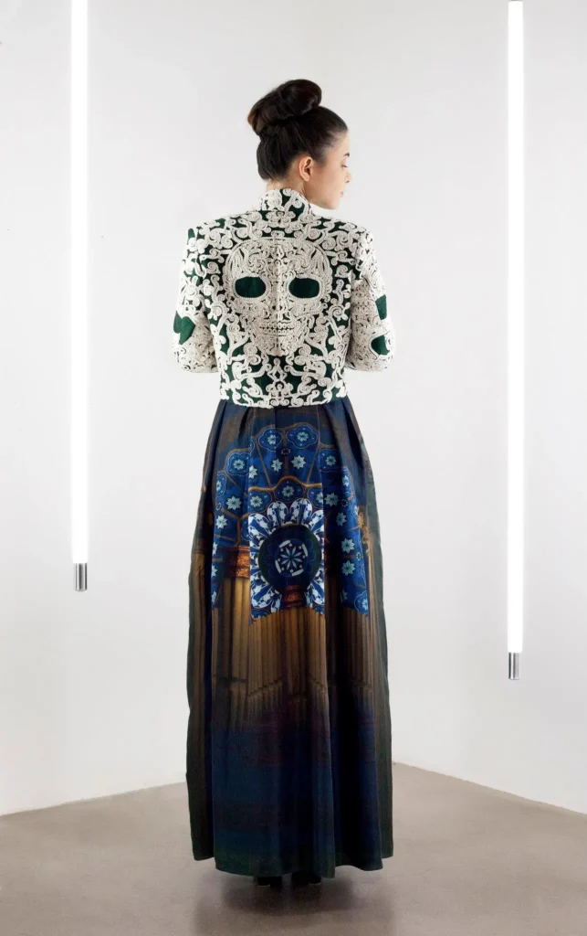Model wearing a cowl-neck printed dress layered with a bolero featuring a large skull motif embroidered on the back.